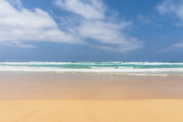 View of the ocean waves, sandy beach and sky.