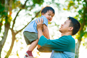 Father hold and lifting little boy in city park sunset light blurred green forest