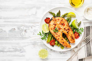 Baked salmon steak garnished with asparagus and tomatoes .