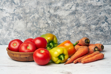 Fresh raw peppers, carrots and tomatoes in wooden bowl on gray textured background
