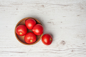 Top view of fresh raw tomatoes in wooden bowl on light wooden background