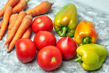 Fresh raw peppers, carrots and tomatoes on gray textured background