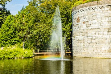 Small fountain with a jet of water reflecting a rainbow in a pond next to the Rondeel (De Vijf Koppen) of the old city wall in the Maastricht city park, sunny day in South Limburg, Netherlands