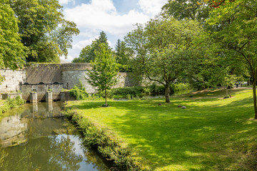 Obraz premium Second medieval old city wall of Maastricht with Reek (waterpoort), water gate on the Jeker river surrounded by trees and green vegetation, sunny summer day in South Limburg, Netherlands