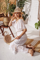 Young elegant fashionable lady wearing summer white crochet jumpsuit, straw hat, heeled sandals,...