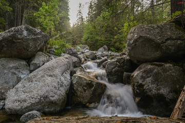 Fototapeta na wymiar Waterfall flows down the stones. Trekking through the mountains along the waterfalls. High Tatras (High Tatras, High Tatras, Magas-Tatras)