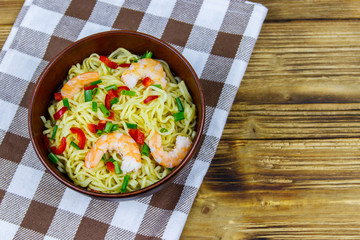 Bowl of instant Chinese noodles with shrimps, green onion and red hot chilli peppers on wooden table. Top view