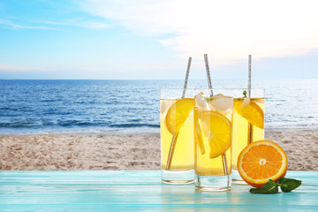 Tasty refreshing drink on wooden table against sandy beach