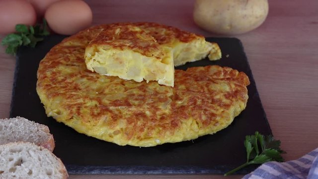 Mano con cuchillo y tenedor cortando un trozo de tortilla de patatas 