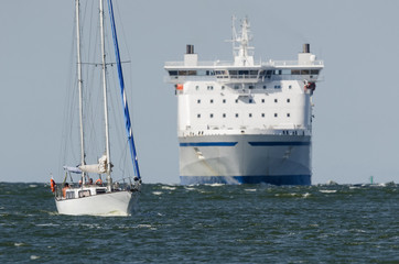 SAILBOAT AT SEA  - A small recreational yacht with a passenger ferry in the background
