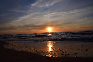Zachód słońca nad morzem z falami w odcieniach mocnego pomarańczu i czerwieni. 