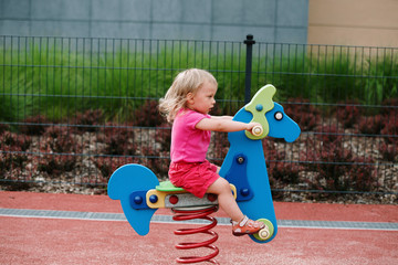 Fototapeta premium baby girl on the child playground, horse riding