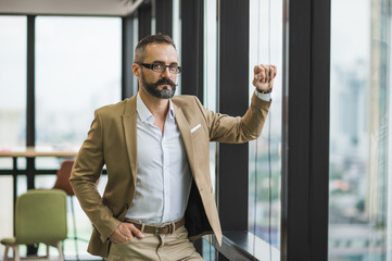 Fototapeta premium Young handsome business bearded man standing post near window in office work place.