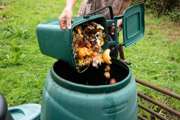A woman emptying a green home composting bin into an outdoor compost bin to reduce waste