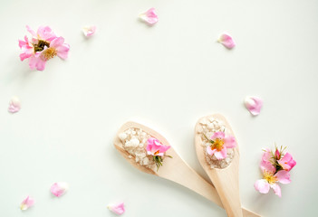 Bath salt in wooden spoons with flowers and rose petals, on a white background. Top view.