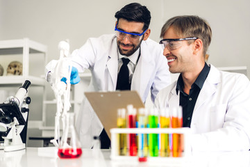 Professional two scientist man research and working doing a chemical experiment while making analyzing and mixing  liquid in test tube.Young science man dropping sample chemical on glass at laboratory