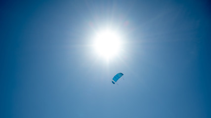 Drachen (Lenkmatte) am blauen Himmel mit der Sonne im Hintergrund