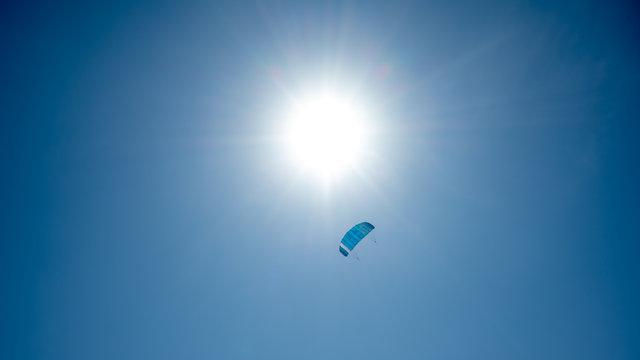 Drachen (Lenkmatte) am blauen Himmel mit der Sonne im Hintergrund