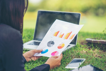Asian entrepreneur business woman reading business graph analyze chart using laptop on green garden...