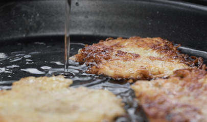 Detailaufnahme von knusprigen Kartoffelpuffer bratend in einer Pfanne in die noch mehr Öl gegossen wird