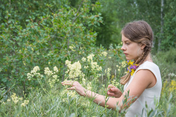 On a summer day, a girl in white flowers stands on the field.