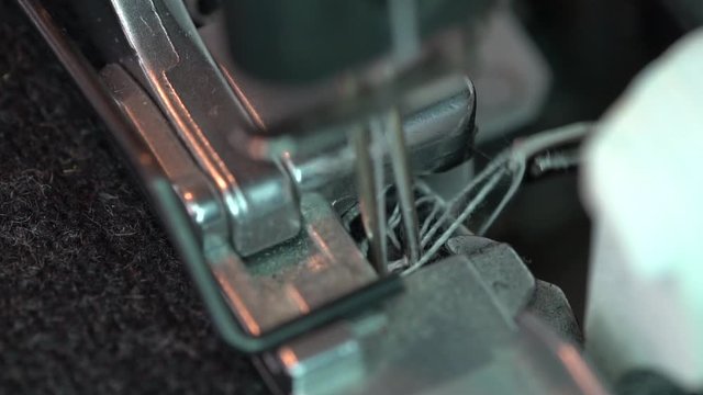 Overlock Sewing Machine. Close up stitches in slow motion. Machine serging the edges of fabric. Presser feet