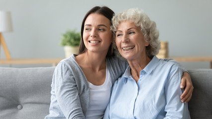 Happy different generations pleasant women cuddling on couch, recollecting positive life moments, enjoying stress free time together indoors, visualizing future or planning weekend vacation.