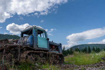 an old abandoned crawler tractor in a field against a cloudy sky, forest and mountains