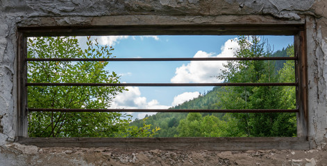 an old window with rusty bars and a beautiful view of the green forest and cloudy sky. Hope for the best