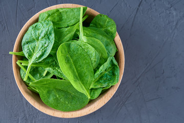 Fresh spinach leaves in wooden bowl on dark background. Organic food