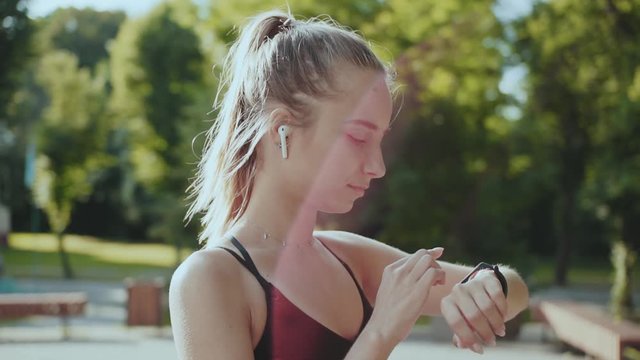 Portrait young fitness woman look at smart watch and camera at sunlight outdoors athlete workout equipment app technology active device slow motion