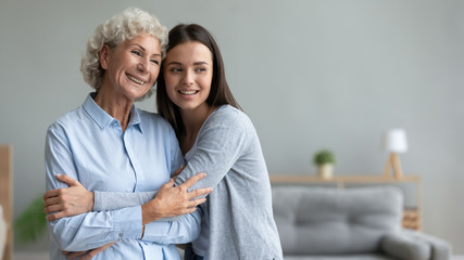 Dreamy young happy beautiful grown up daughter cuddling middle aged sincerely smiling older mature...