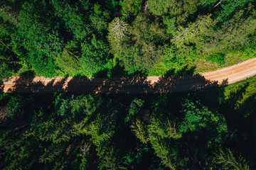 Aerial shot of a long road surrounded by green forest in Latvian countryside..