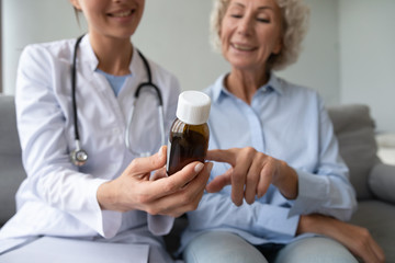 Focus on glass bottle with treatment capsules in female doctor hands. Pleasant young gp doc helping middle aged woman with pills, prescribing healthcare multi vitamins complex. reading instructions.