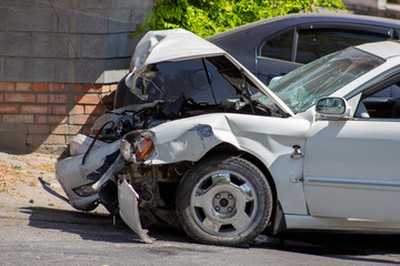 A road accident, a car that crashed, a white car on the road, cracks in the glass and a damaged bumper.