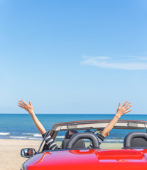 A woman in a red car raised her hands up at the seaside.
