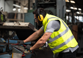 Portrait of technician man or industrial worker with hardhat or helmet, eye protection glasses and vest working electronic machinery on laptop and mechanical  in Factory of manufacturing place