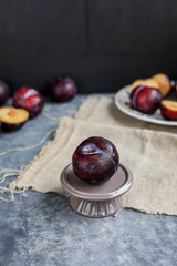 Red plums on a vintage plate on a gray background. Pieces of fruit. View from above.