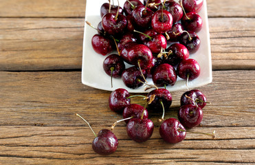 Fresh Cherry fruit in white dish and some cherry fall out dish on old wooden table