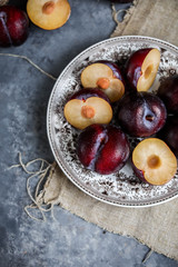 Red plums on a vintage plate on a gray background. Pieces of fruit. View from above.