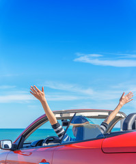 A woman in a red car raised her hands up at the seaside.