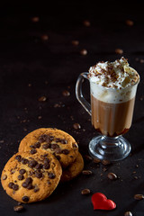 Close up of a glass cup of coffee with whipped cream and chocolate on it, chocolate chip cookies...