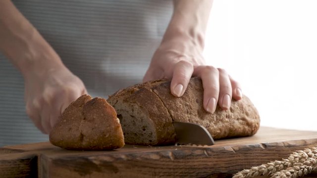 Slicing brown sourdough rye and wheat bread on wooden cutting board. Female hands slice bread with bread knife