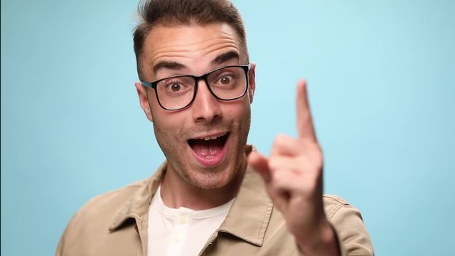 attractive casual guy fixing his glasses, scratching his head and wondering about something then being happily surprised by an great idea and celebrating succes on blue background