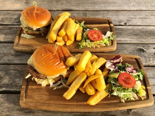 Burger, hamburger with french fries, ketchup, mustard and fresh vegetables on a cutting wooden board.