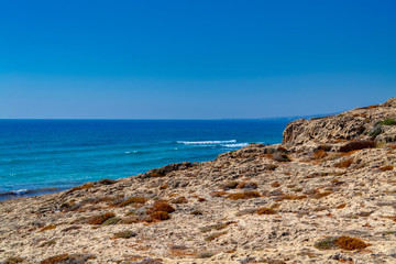 Rocks on the sea coast in the city of Paphos, Cyprus.  View of the yellow sand and stone cliffs with shallow desert vegetation.