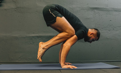 Sporty young man working out, doing handstand yoga. Studio shot in urban fitness gym with grey background for copy space.