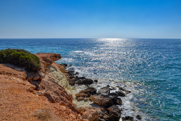 Fototapeta na wymiar View of the blue water of the Mediterranean Sea and coastal cliffs on the coast of the island of Cyprus. Sunny hot day at the coastline near the town of Paphos.