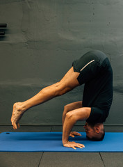 Sporty young man working out, doing handstand yoga. Studio shot in urban fitness gym with grey background for copy space.