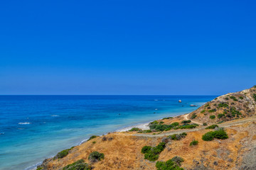 Fototapeta na wymiar View of the Aphrodite's beach from the mountain observation platform on a sunny hot day. The famous beach on the island of Cyprus, near the town of Paphos.